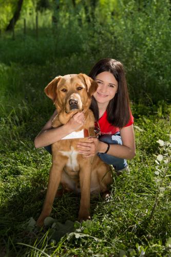 Lou se tenant accroupie dans l'herbe et tenant dans ses bras Pita, son chien guide d'aveugle, labrador croisé golden sable.