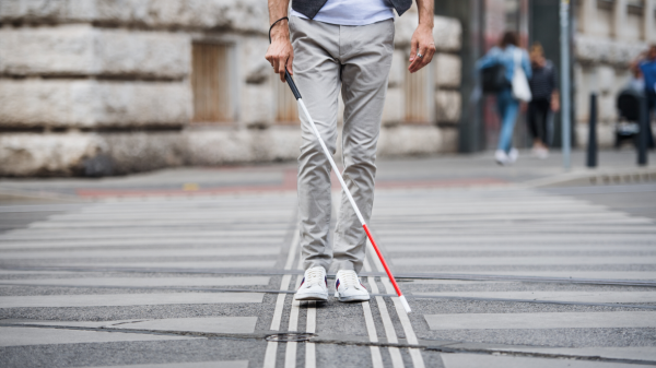 Un homme avec une canne marche sur un passage piéton 